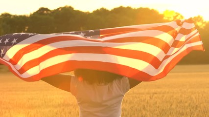 4K video clip of mixed race African American girl teenager female young woman holding an American USA Stars and Stripes flag in a wheat field at sunset or sunrise