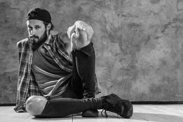 Posing tutorial. Monochrome shot of bearded guy sitting with his legs crossed pointing at the camera. - Powered by Adobe