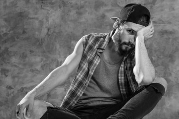 A bit tired. Black and white shot of a manly bearded hipster sitting looking to the camera.