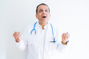 Middle age doctor man wearing stethoscope and medical coat over white background celebrating surprised and amazed for success with arms raised and open eyes. Winner concept.