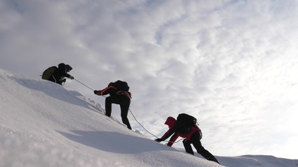 Travelers climb rope to their victory through snow uphill in strong wind. tourists in winter work...