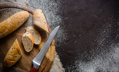 Sliced bread on the board. Dark brown background. Knife, crumbs and flour. Place for text.