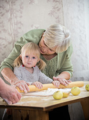 Obraz premium A grandmother making little pies with her granddaughter. Rolling the dough