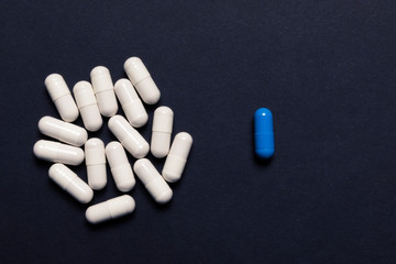 A bunch of white pills and one blue on a dark background