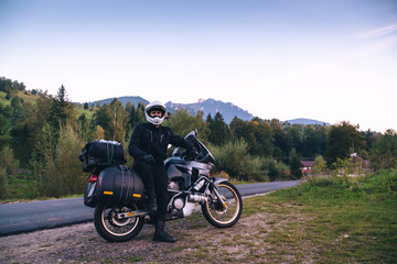 Fototapeta na wymiar Rider Man and off tourism adventure motorcycles with side bags and equipment for long road trip, travel touring concept, Ceahlau, Romania, mountains on background, sunset evening