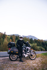 Fototapeta na wymiar Rider Man and off tourism adventure motorcycles with side bags and equipment for long road trip, travel touring concept, Ceahlau, Romania, mountains on background, sunset evening, vertical photo