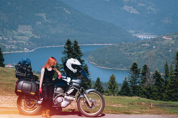 Fototapeta premium woman biker with adventure motorcycle on road, Ceahlau mountains, Romania, tourism travel concept, motorcyclists way, copy space, lake Lzvorul Muntelui, beautiful sunny day
