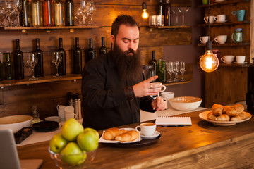 Beaded hipste waiter preparing cofffe behind the bar.