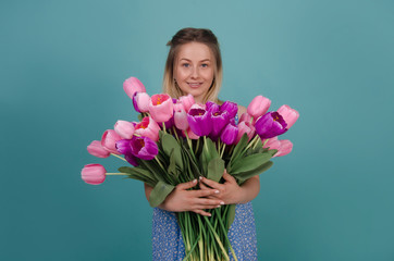 Smiling woman with bouquet of pink and purple tulips. Smiling woman with bunch of flowers in her hands in blue dress. Summer and spring concept. Isolated on blue background