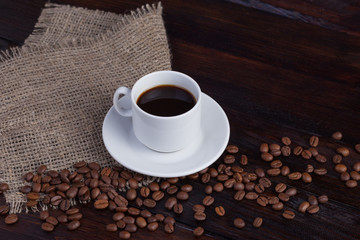 White cup of coffee with coffee grains near on linen fabric on the dark vintage background