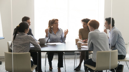 Middle-aged businesswoman speaking at diverse group negotiations at conference table