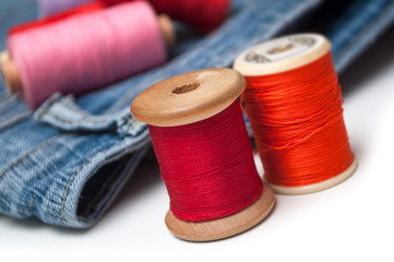 closeup of colorful sewing thread spool bobbins on white table on blue jeans background