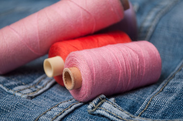 Fototapeta na wymiar closeup of colorful sewing thread spool bobbins on blue jeans background