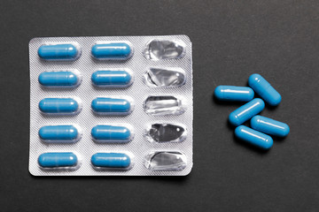 Blue pills in a pack and a handful next to a black background