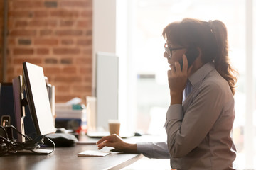 Serious businesswoman talking on phone using computer in office