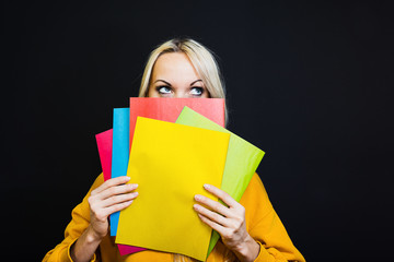 The image of a student girl, hiding her face behind the books, the look thoughtfully directed upwards.  Stands on a black background.  The concept of school, University.