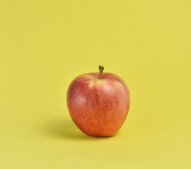 Fresh red apple fruit on vibrant yellow foam mat background.