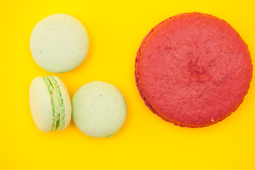 Big Sweet raspberries macaron next to little macaroons over yellow background
