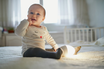 Adorable baby girl playing with bedside lamp in nursery