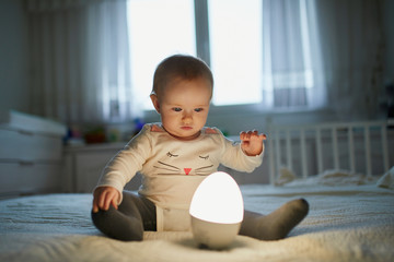 Adorable baby girl playing with bedside lamp in nursery