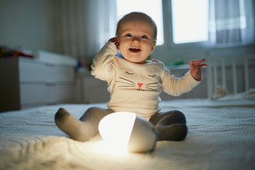 Adorable baby girl playing with bedside lamp in nursery
