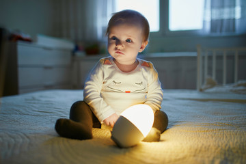 Adorable baby girl playing with bedside lamp in nursery