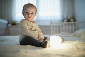 Adorable baby girl playing with bedside lamp in nursery