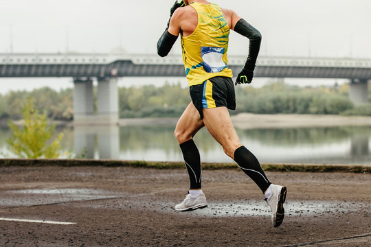 Male Runner In Compression Socks And Protective Arm Sleeves Run River Embankment