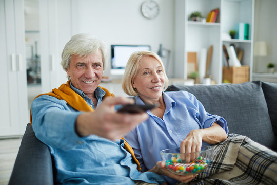 Portrait of contemporary mature couple watching tv at home and using remote control, copy space
