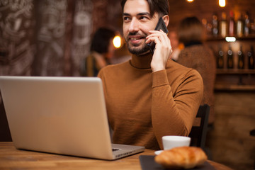 Executive businessman talking on the phone while working on his laptop in a coffee shop