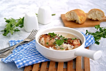 Fried chicken in a creamy garlic sauce or chkmerili chicken in a portioned ceramic pan on a light gray background. Georgian cuisine. Selective focus.