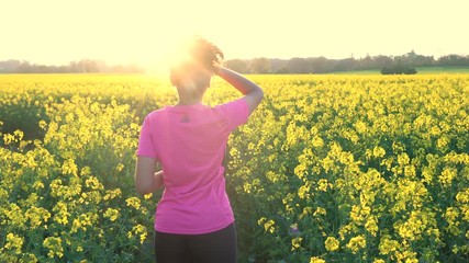 Beautiful healthy mixed race African American girl teenager female young woman resting drinking from water bottle after running or jogging in field of yellow flowers