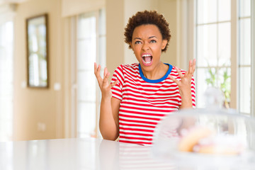 Young beautiful african american woman at home crazy and mad shouting and yelling with aggressive...
