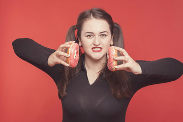 Model plus size with sweet donut, happy girl smiling holding in hands donuts and push them, in black bodysuit. XXL female on red background