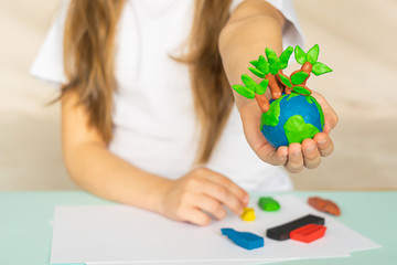 A small globe with trees in the hands of a child. Layout of the planet made of plasticine in...