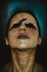 Creepy close-up portrait of young woman without eyes on dark background