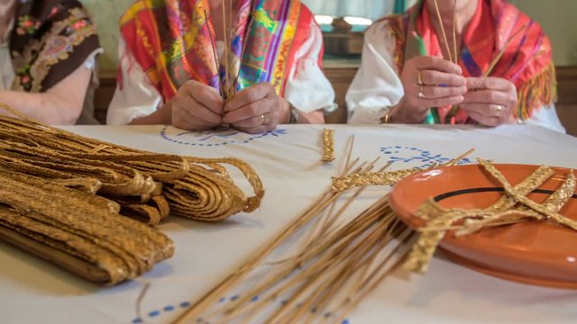 Three senior ladies are doing something out of wheat ears and they are singing at the same time. They're also wearing scarfs.