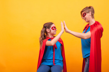 Mother and daughter dressed like superheros giving hi5 over yellow background.