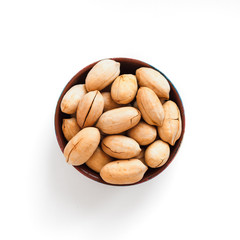 pecan nuts in brown clay bowl on white background, top view
