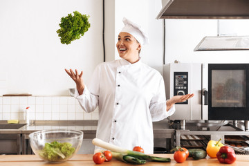 Photo of european woman chef wearing white uniform cooking meal with fresh vegetables, in kitchen at the restaurant