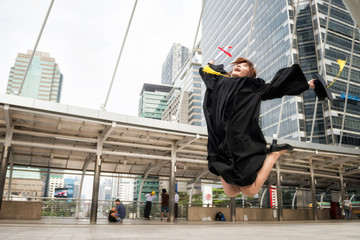 Asian graduate woman in gown jump with diploma