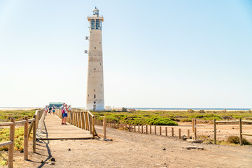 Fototapeta na wymiar Lighthouse and wooden bridge with tourists in Morro Jable, Fuerteventura, Spain