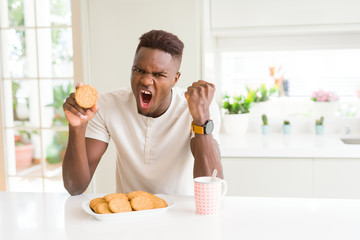 African american man eating healthy whole grain biscuit annoyed and frustrated shouting with anger, crazy and yelling with raised hand, anger concept