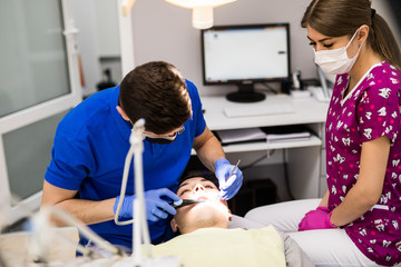 Male dentist with assistant examining girls teeth in the dentists chair. Dental clinic