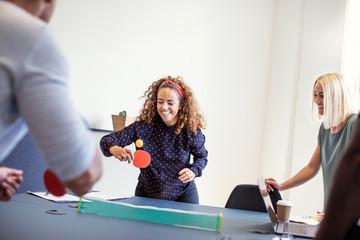 Laughing coworkers playing table tennis on an office table
