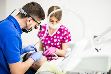 Obraz premium Male dentist and female assistant checking up patient teeth with dental tools microscope, mirror and probe at dental clinic office. Medicine, dentistry and health care concept. Dental equipment