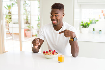Young african american man eating healthy breakfast in the morning very happy pointing with hand and finger