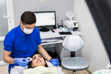 Fototapeta premium Man dentist and woman patient during the process of teeth whitening in dental clinic