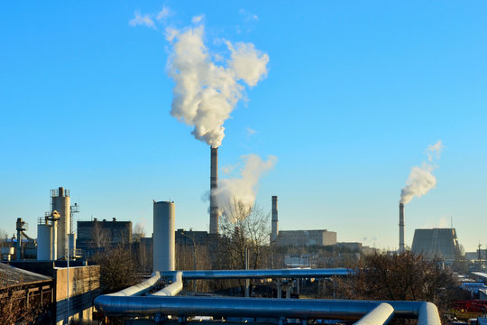 Smoke tower of CHP and blue sky. Central Electric Heat. Outside pipelines near Combined Heat and Power. Industrial zone of plants, electrical wires. Industrial pipelines on pipe-bridge