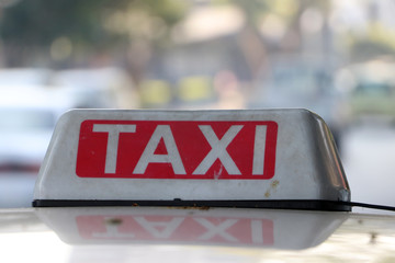 Taxi light sign or cab sign in drab white and red color with white text on the car roof at the street.